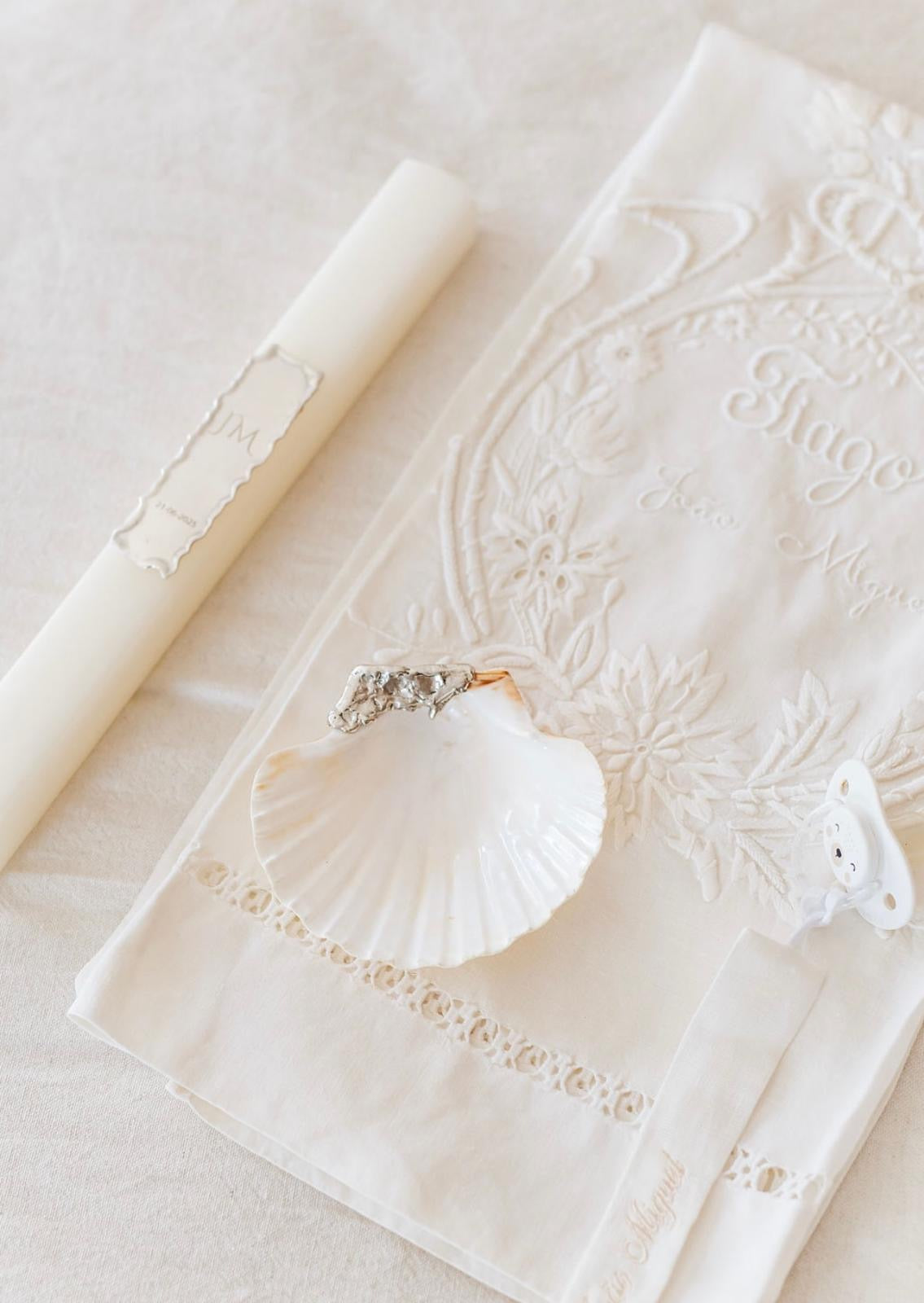 Concha de batizado com aplicação em prata e vela com placa gravada, sobre toalha bordada